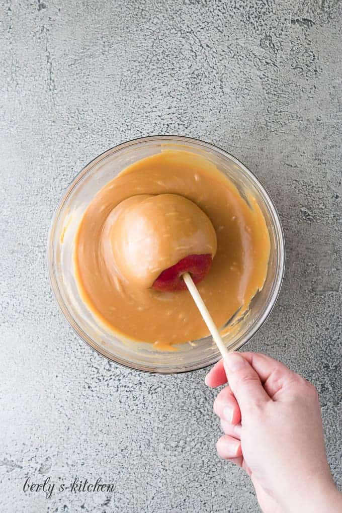 The apple being spun in the caramel for even distribution.