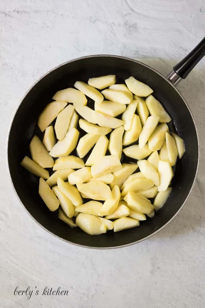 Peeled apple slices in a large skillet with melted butter.
