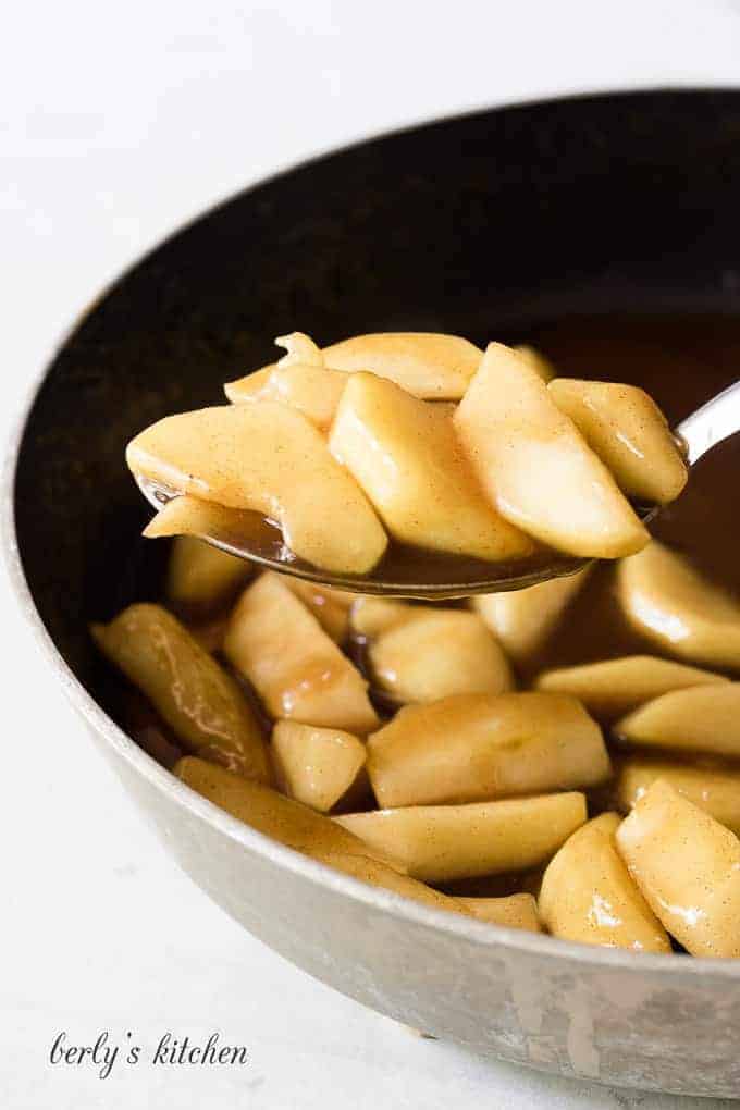 A large metal spoon scooping out the finished cinnamon apples.