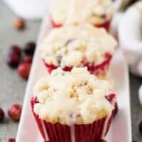 Three cranberry orange muffins drizzled with glaze on a plate.