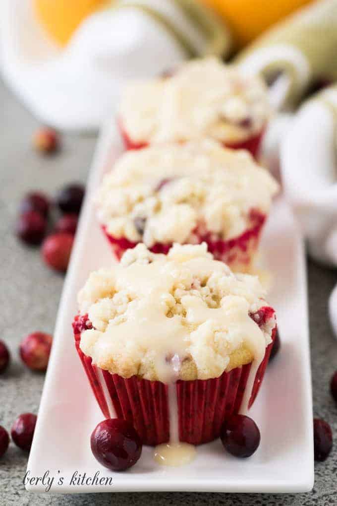 Three cranberry orange muffins drizzled with glaze on a plate.
