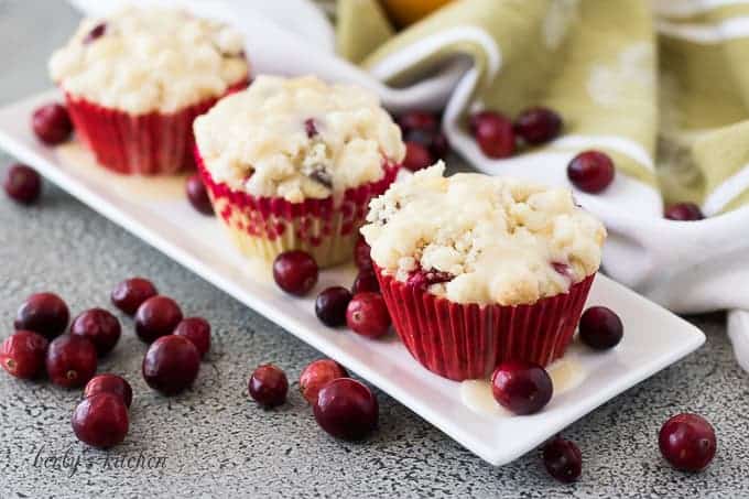 Three cranberry orange muffins on a plate topped with glaze.