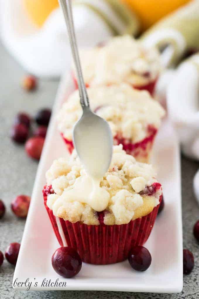 The sweet glaze being drizzled over the finished cranberry muffins.