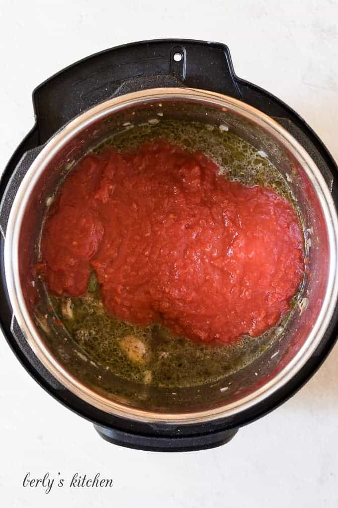 Broth and tomatoes being added to the ground beef mixture.