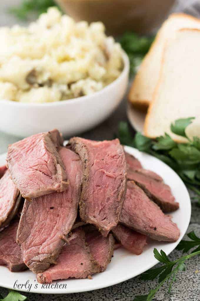 Mashed potatoes, bread, and sliced beef in separate white dishes.