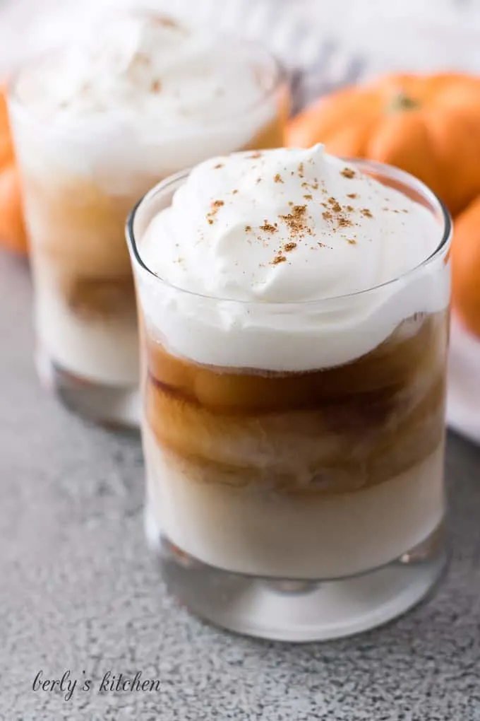 Two cocktails garnished with whipped cream and pumpkin pie spice.