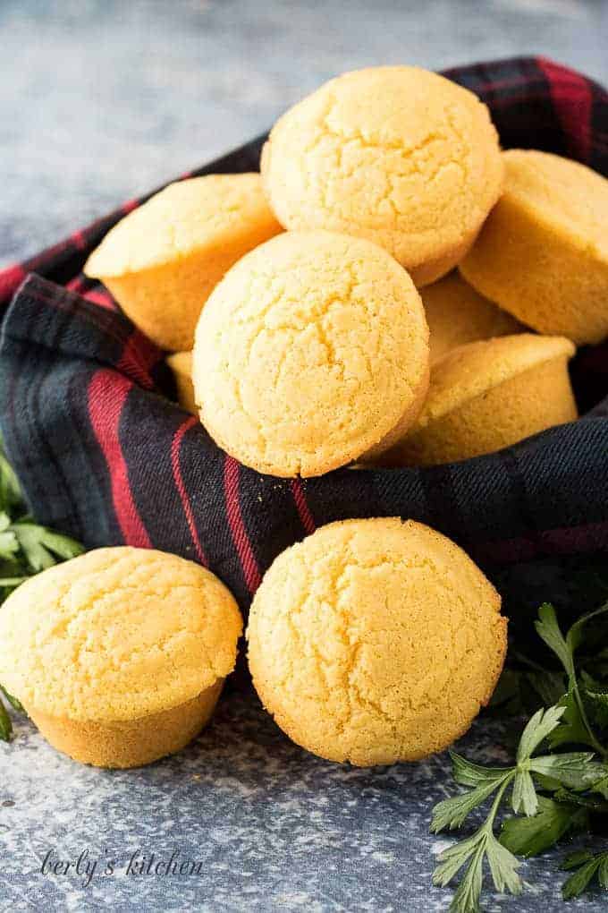 Eight cornbread muffins stacked in a bowl with a towel.