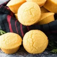 Homemade cornbread muffins in a bowl with a decorative towel.