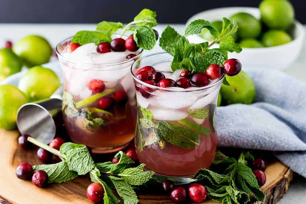 Two cranberry cocktails served with fresh cranberries and fresh mint.