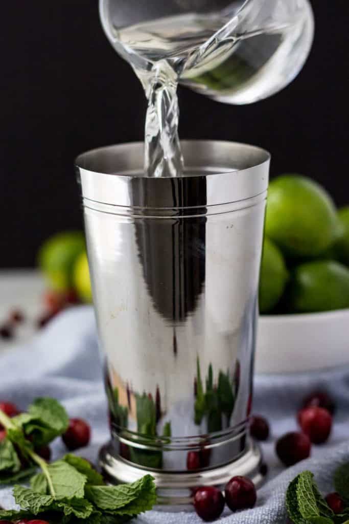 A large metal cocktail shaker being filled with simple syrup.