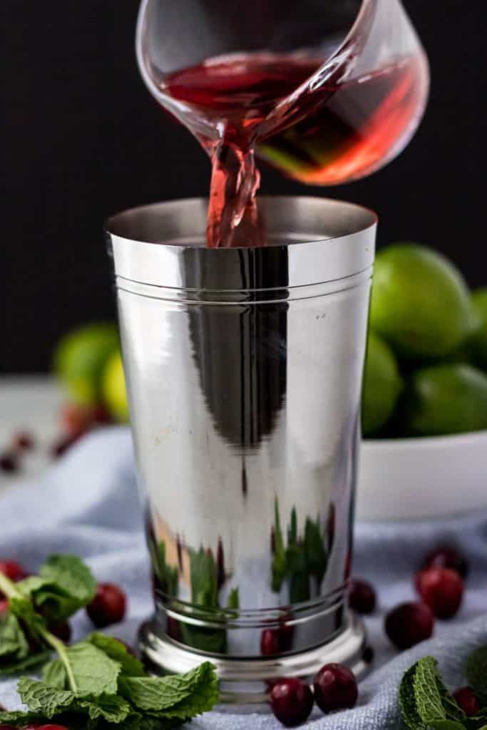 The cranberry juice being poured into the metal cocktail shaker.