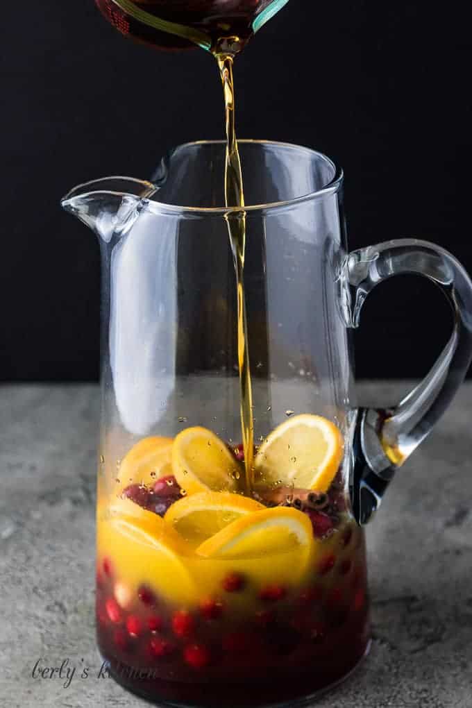 Brandy being poured into a pitcher with wine and fruit.