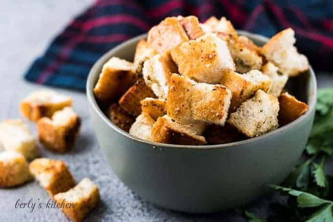 A small green bowl filled with buttery seasoned homemade croutons.