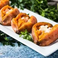 Four sweet potatoes cut open and topped with melting butter.