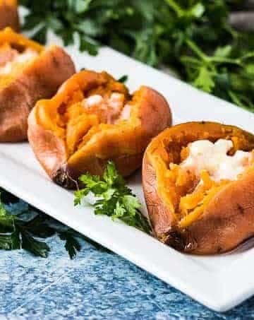 Four sweet potatoes cut open and topped with melting butter.