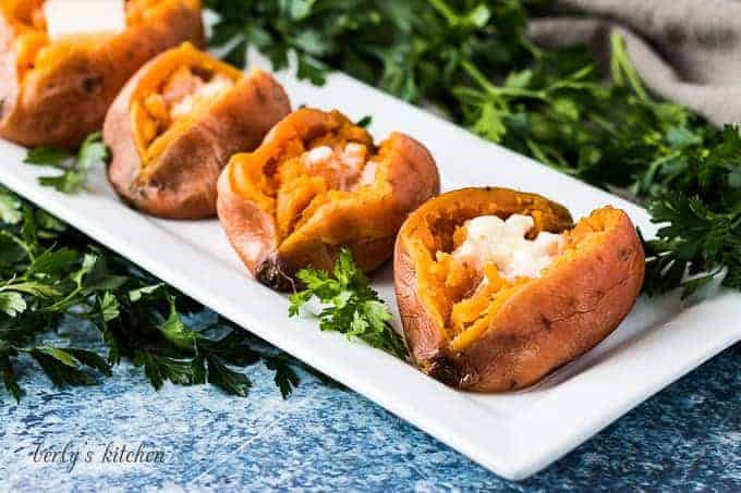 Four sweet potatoes cut open and topped with melting butter.