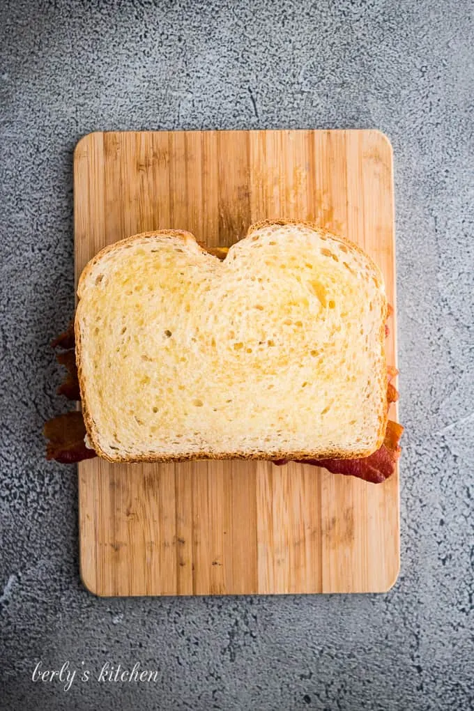 A buttered slice of sourdough atop the bacon and cheeses.