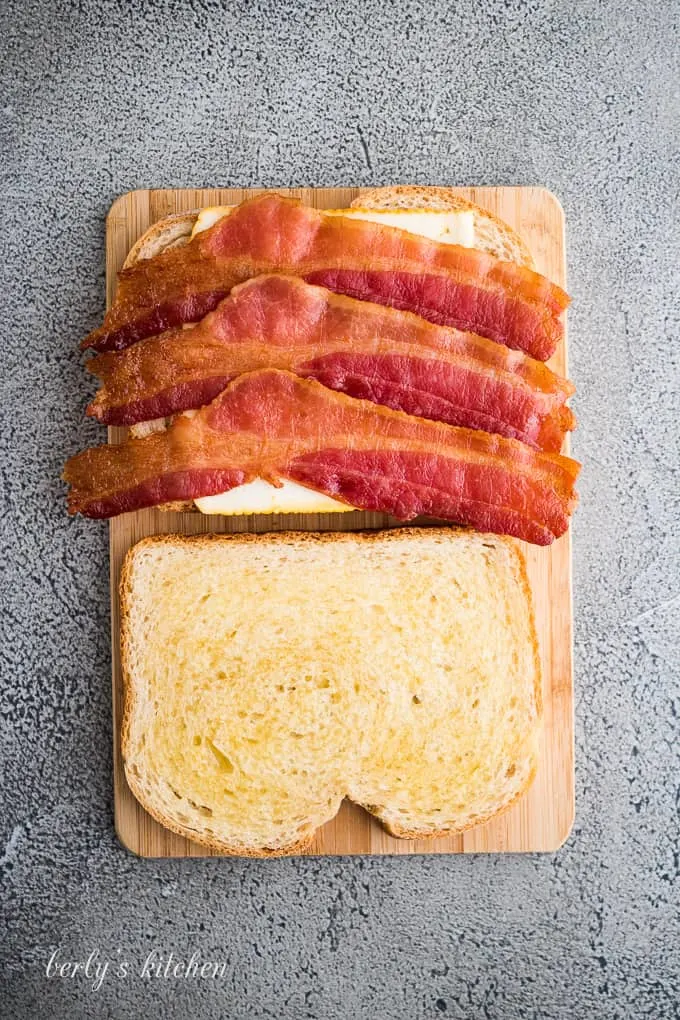 A slice of buttered sourdough with cheese and cooked bacon.