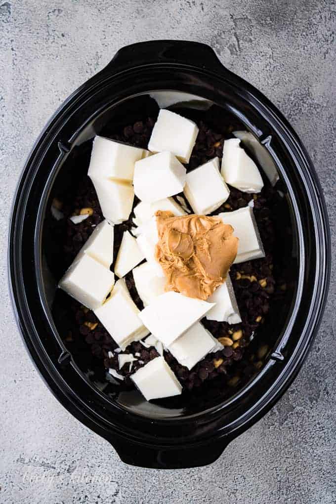 Almond bark, peanuts, and other ingredients layered into a crockpot.