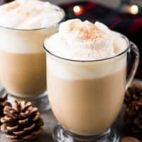 Two eggnog lattes served in clear mugs with whipped cream.