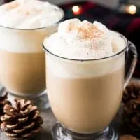 Two eggnog lattes served in clear mugs with whipped cream.