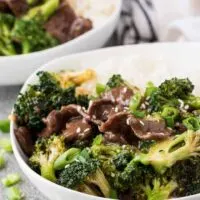 Two bowls of beef and broccoli served with steamed rice.