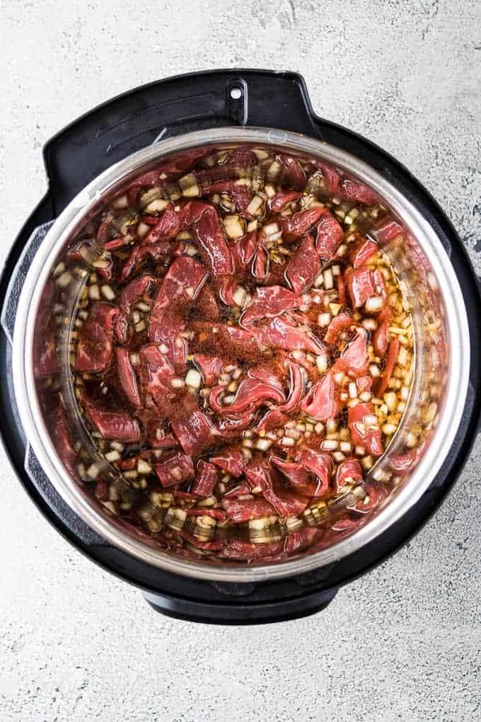 Uncooked beef and sauce in the pressure cooker liner.