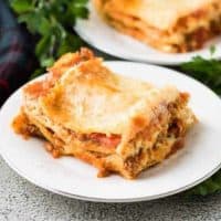 Two squares of lasagna on small plates garnished with parsley.