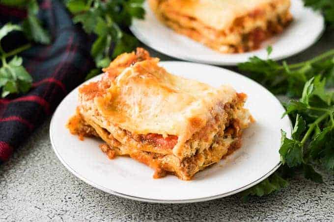 Two squares of lasagna on small plates garnished with parsley.