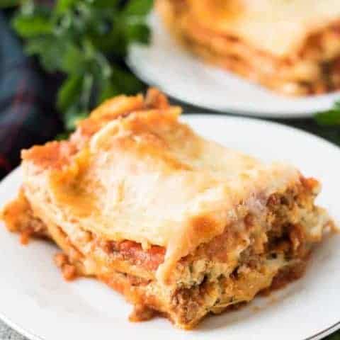Slices of lasagna on small plates surrounded by fresh parsley.