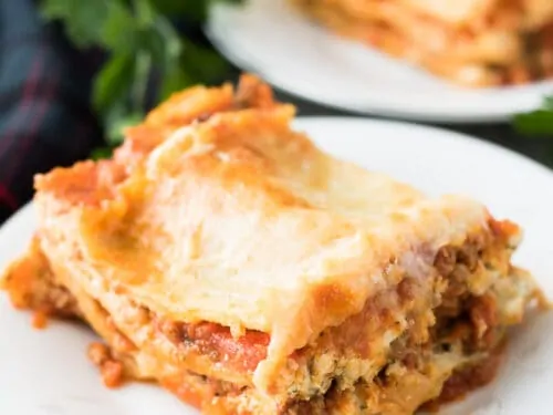 Slices of lasagna on small plates surrounded by fresh parsley.