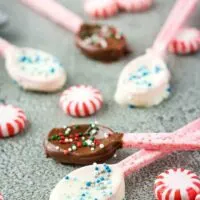 Five chocolate dipped candy spoons surrounded by multiple peppermint candies.