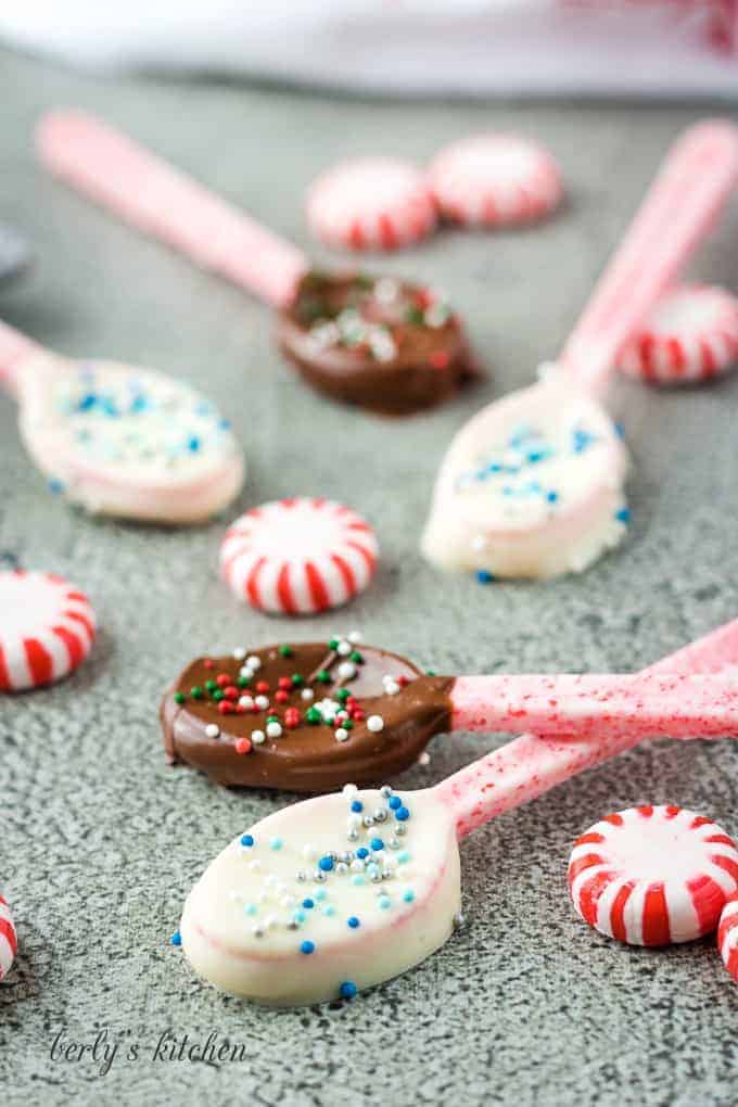 Five chocolate dipped candy spoons surrounded by multiple peppermint candies.