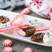 Six chocolate dipped peppermint spoons on a rectangular white plate.