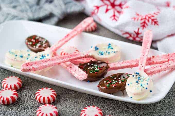 Six chocolate dipped peppermint spoons on a rectangular white plate.