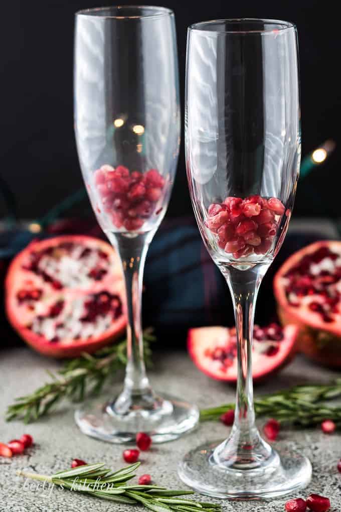 A handful of pomegranate seeds inside two tall champagne glasses.