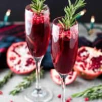 Two pomegranate mimosas served in champagne glasses garnished with rosemary.