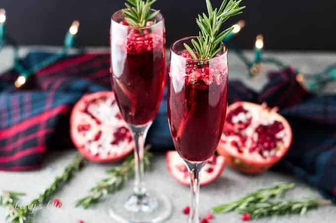 Two pomegranate mimosas served in champagne glasses garnished with rosemary.