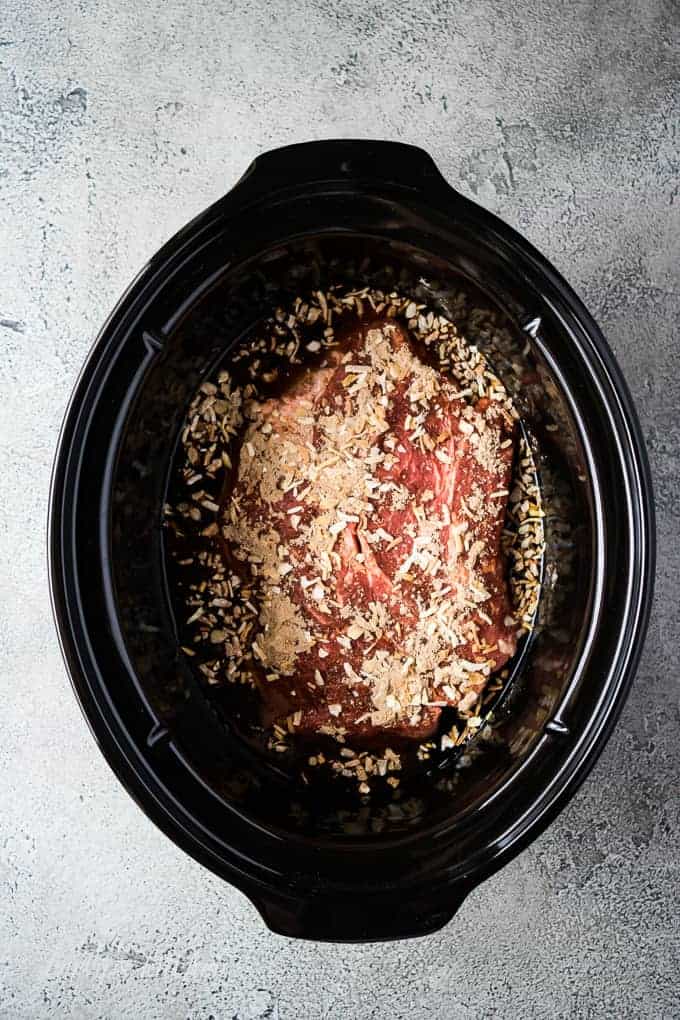 A seasoned beef roast sitting in a large slow cooker.