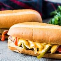 Two philly cheesesteak sandwiches with provolone or cheddar cheese sauce.