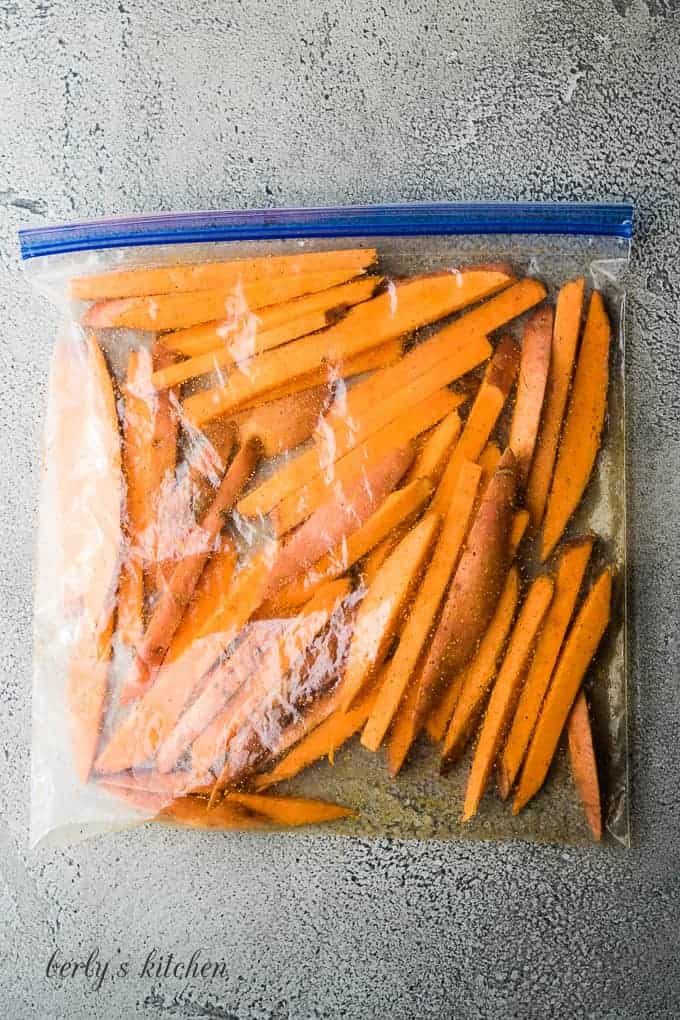 Sweet potato slices coated with seasoning and olive oil in a closed zip bag.
