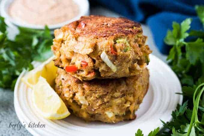 Two crab cakes on a plate with a lemon wedge.
