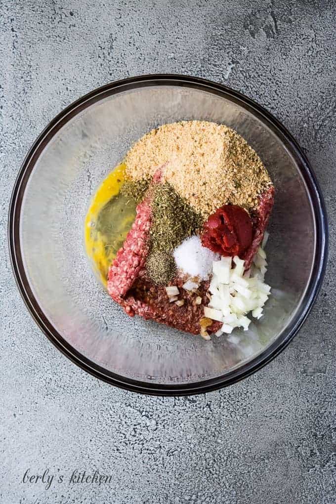 Ground beef and other ingredients in a large glass mixing bowl.