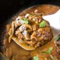 One cooked salisbury steak being lifted from the slow cooker.