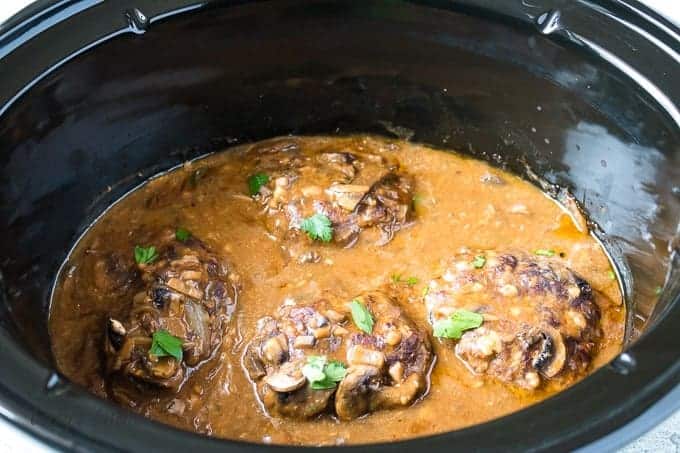 Four large salisbury steaks in a crockpot with mushroom gravy.