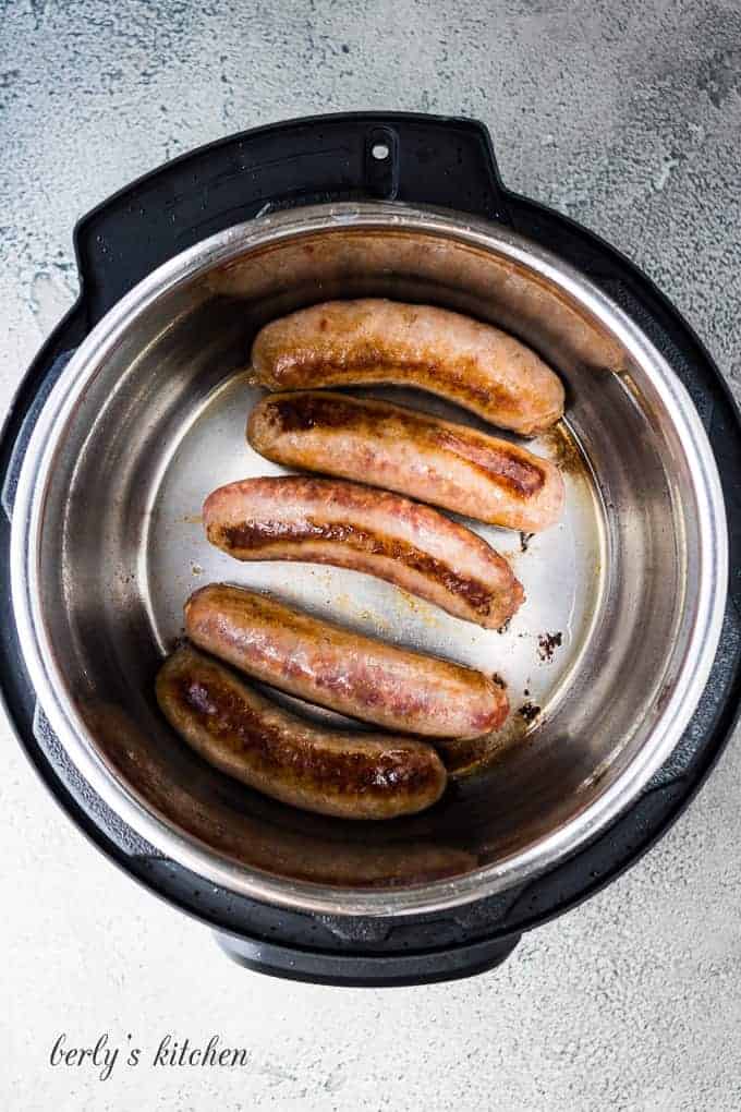 Five Italian sausage links sauteing in the preheated pressure cooker.