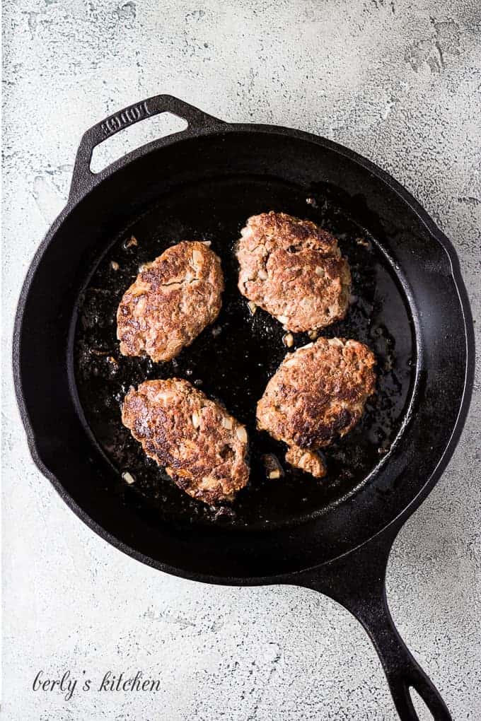 The beef mixture formed into patties cooking in the skillet.