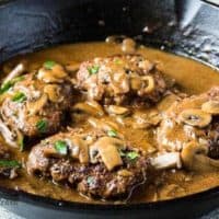 Four Salisbury steaks covered in gravy sitting in a skillet.
