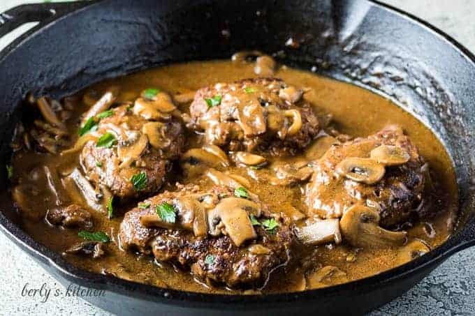 Four Salisbury steaks covered in gravy sitting in a skillet.