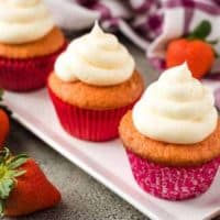 Three strawberry champagne cupcakes in red liners on a plate.